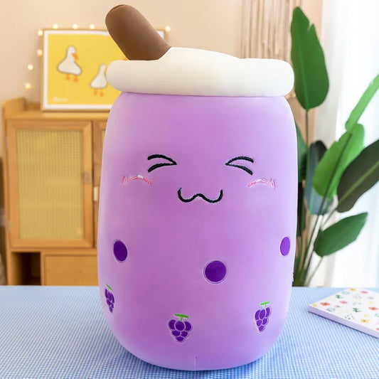 A purple plushie toy resembling a boba drink with a smiling face, purple grape icons, and a brown straw