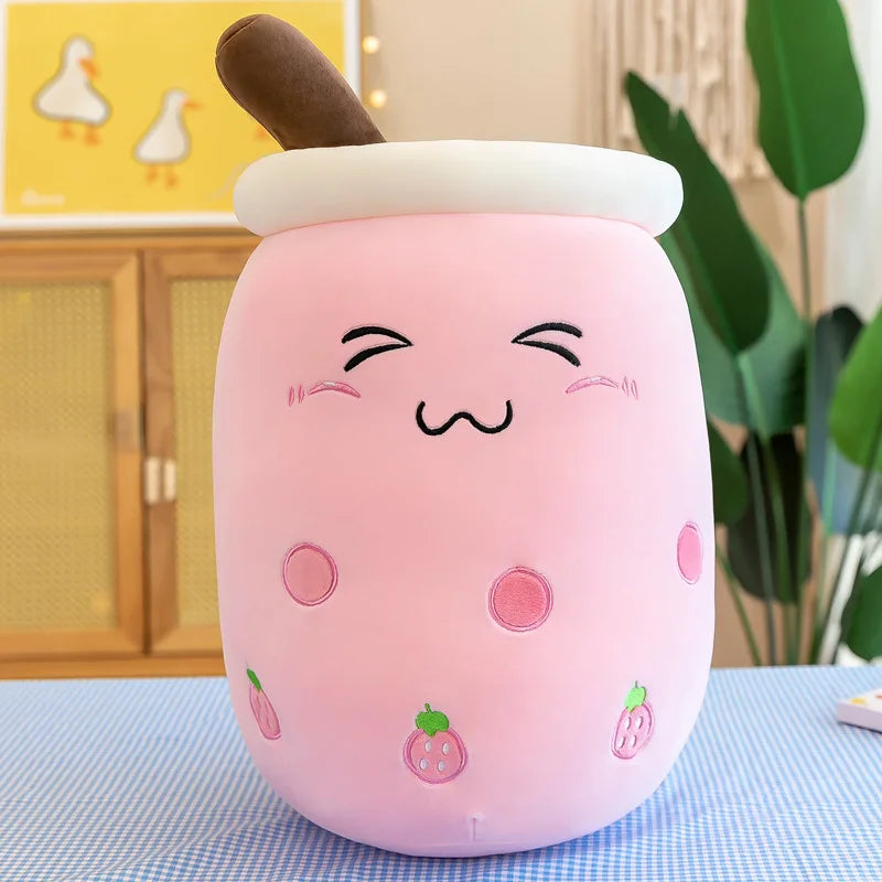 An image showing a pink boba tea plushie doll with a blushing face, pink cheeks, a coy smile, strawberry icons on the side of the cup, and a brown straw