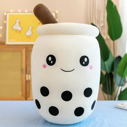 An image of a white bubble tea plushie with black tapioca pearls, a smiling cute face with pink dimples, and a brown straw at the top