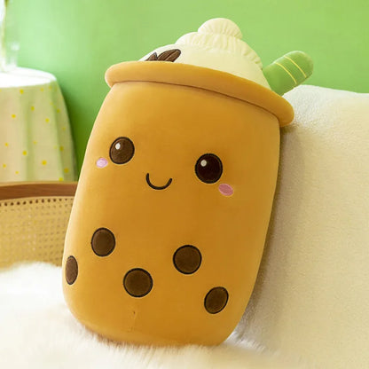 An image of a maple-brown boba tea coffee plushie with five black boba balls, a smiling face, a white cream foam with two coffee beans and a green straw