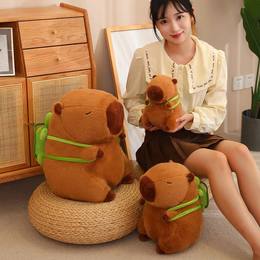 An image depicting a bedroom with 3 plushie capybaras, ranging in size from large, medium, and small with a lady sitting on a cushion holding the smallest capybara.