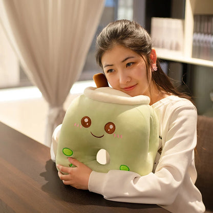 The image shows a girl sitting at a table embracing the smiling green apple boba tea plushie pillow with center hole.