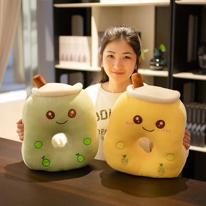 The image shows a girl sitting at a brown table holding two bubble tea pillows with center holes comprising the green apple color and yellow pineapple color.