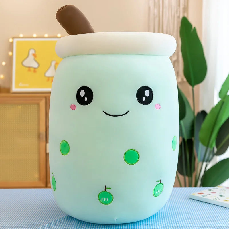 A smiling green bubble tea plushie with green apple icons, a smile, two big black eyes, and a brown straw