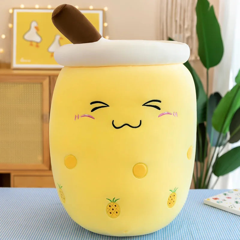 An image showing a yellow pineapple boba tea plush with small pineapple icons on the side of the cup, a blushing face, and a brown straw