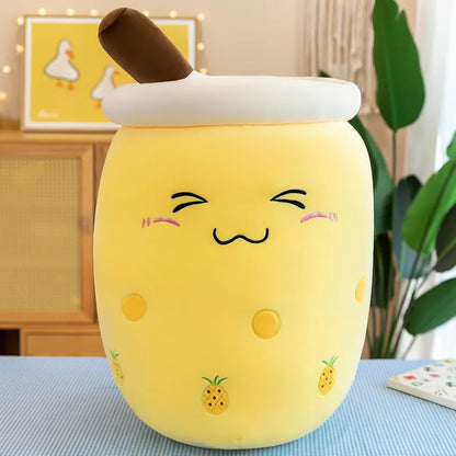 An image showing a yellow pineapple boba tea plush with small pineapple icons on the side of the cup, a blushing face, and a brown straw