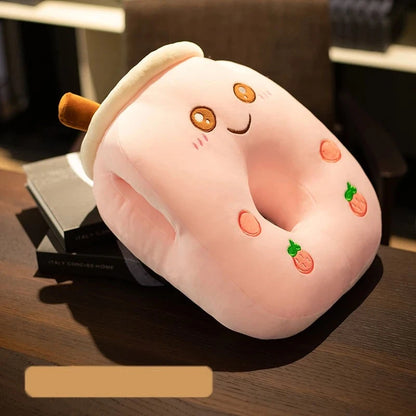 A pink pillow with a smiling face, two strawberries, two small pink circles, a center hole, two side holes, and a brown straw, on a desk.