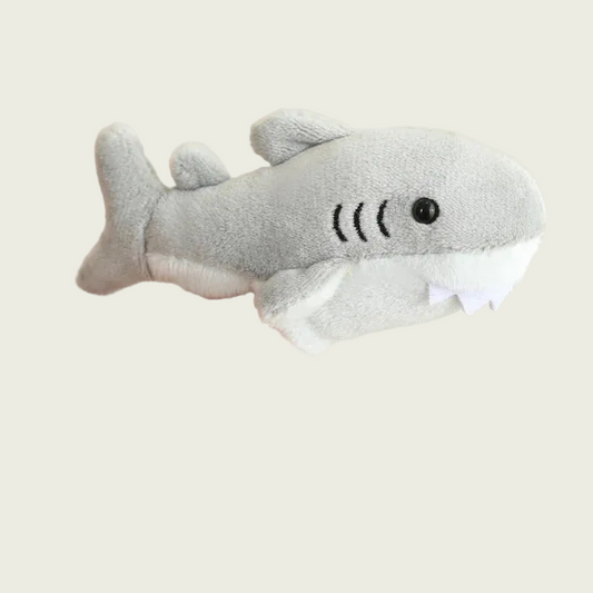 Plush shark toy held in a hand against a beige background