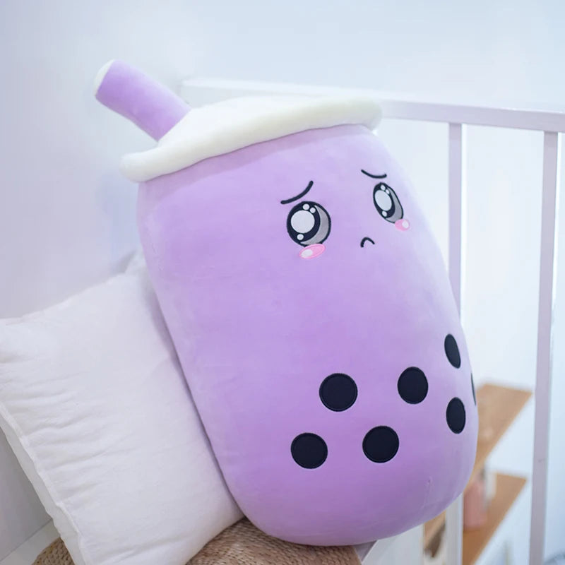 An image of a purple taro boba tea plushie doll with a sad face, welled up eyes with tears, upside down eyebrows and black balls representing tapioca