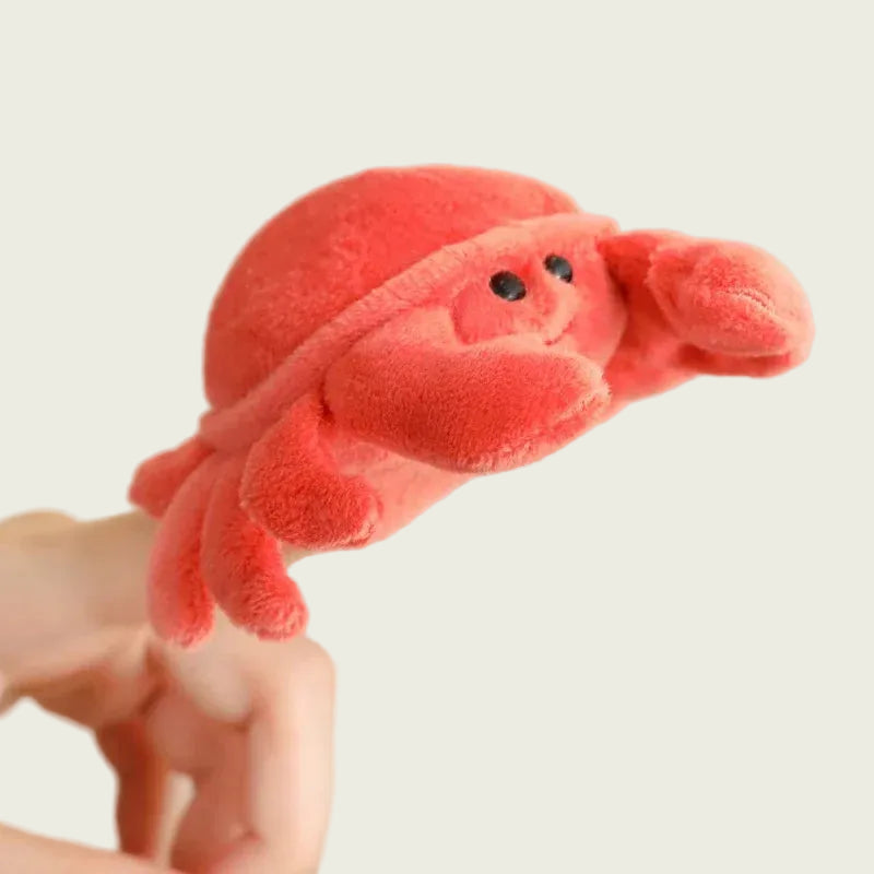 Red plush crab toy puppet held by a finger against a plain background
