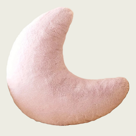 Pink waning crescent moon-shaped plush pillow on a light gray sofa with a plant in the background