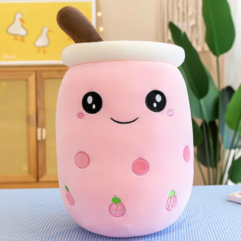 Product image of a pink smiling bubble tea plushie doll, with small strawberry graphics on the side of the plushie and a brown straw