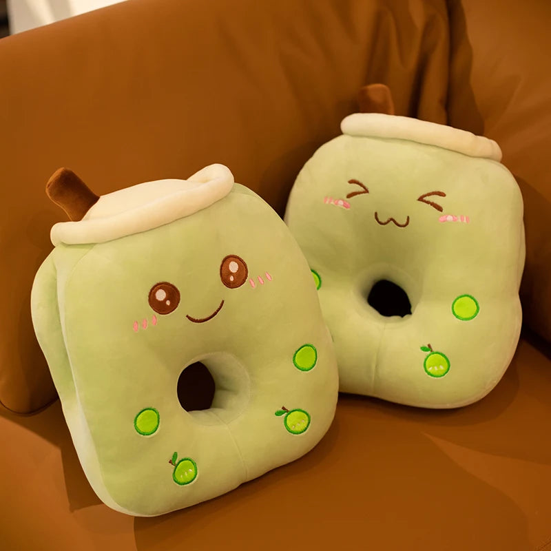 The image shows two green apple plushie pillows, one smiling and one grinning, on a brown sofa.